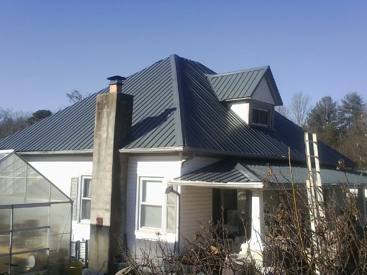 Dark blue standing seam metal roof on a white farmhouse with dormer in Fontana