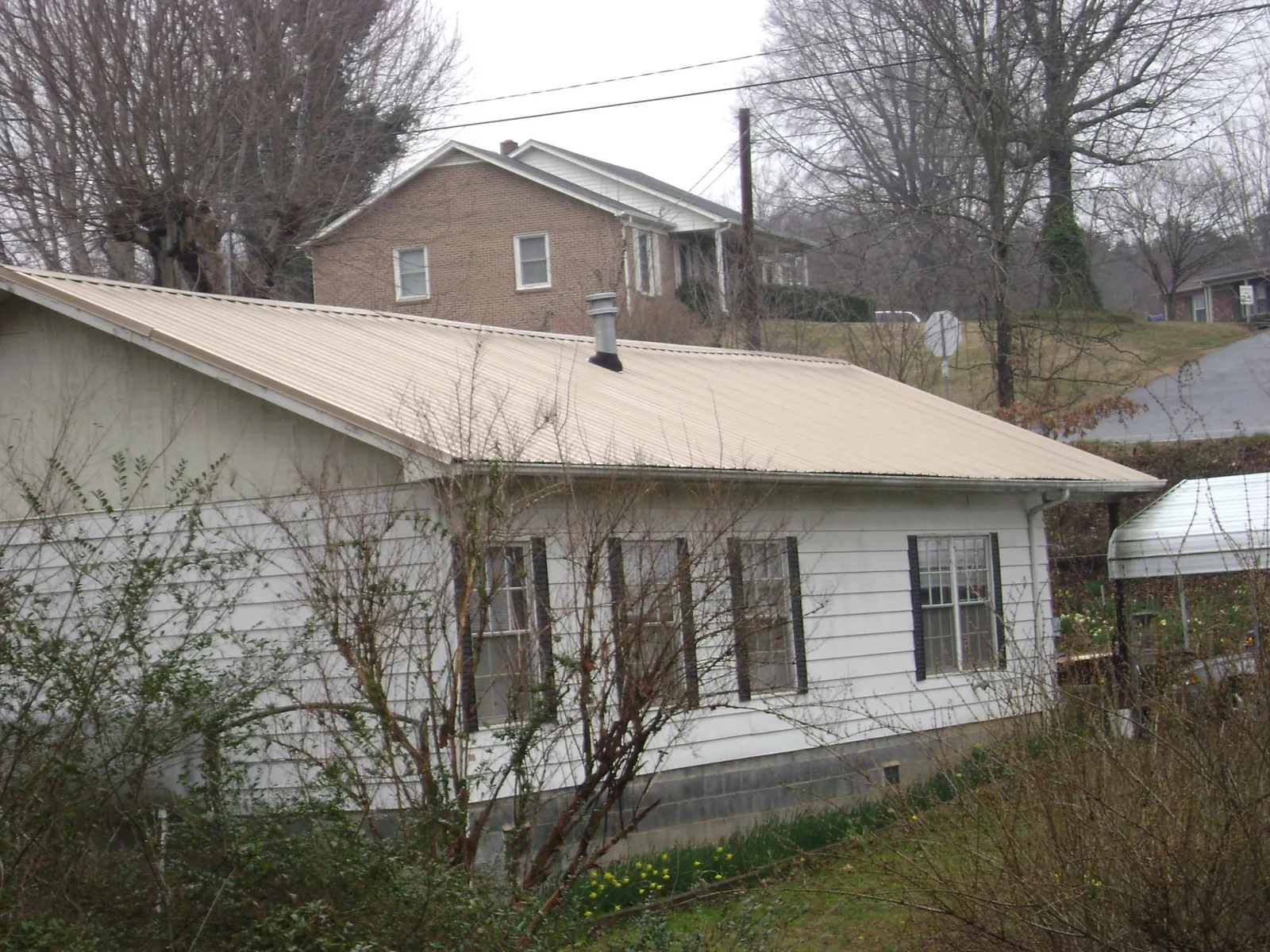 Tan metal roof on a white sided house set into a hillside — Commercial Roofing by Roofing Brothers in Fontana